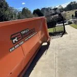 Large orange dumpster in homeowners driveway to fill up for moving day.