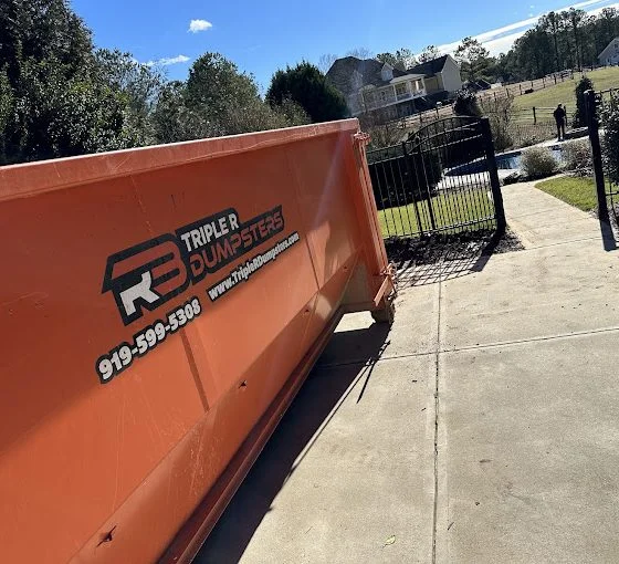 Large orange dumpster in homeowners driveway to fill up for moving day.