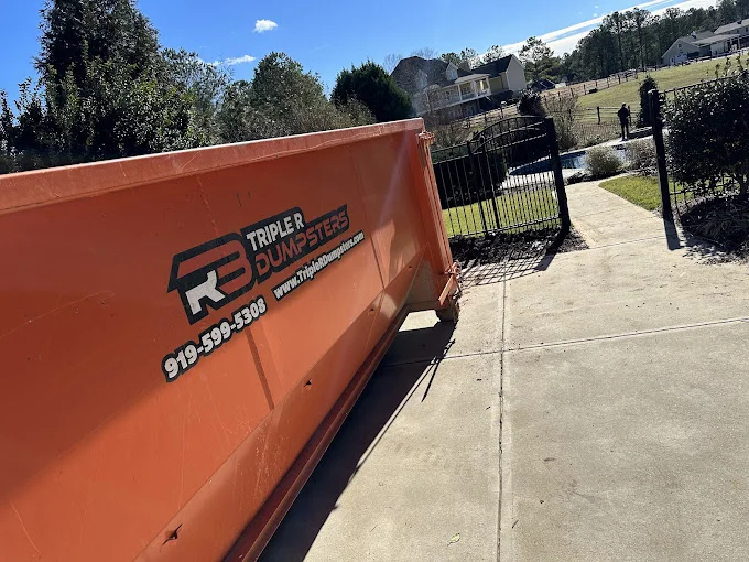 Large orange dumpster in homeowners driveway to fill up for moving day.